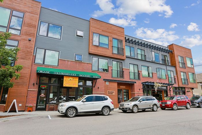 Vibrant urban apartment with modern facade, featuring large windows and charming brickwork, set above lively retail spaces.