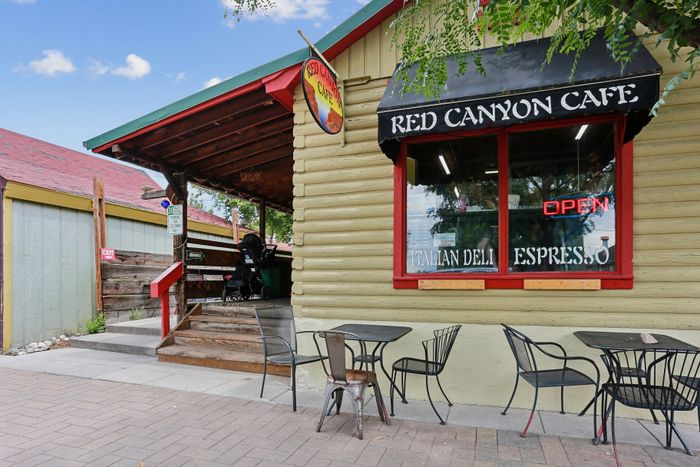 Charming Red Canyon Cafe with inviting outdoor seating and a welcoming open sign, offering Italian deli delights and espresso.