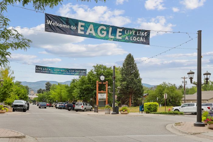 Charming small-town street in Eagle with welcoming banners, lush greenery, and a picturesque mountain backdrop.
