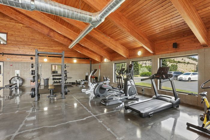 Spacious and modern fitness center with high-end equipment and panoramic views, featuring a wooden beam ceiling and polished concrete floors.