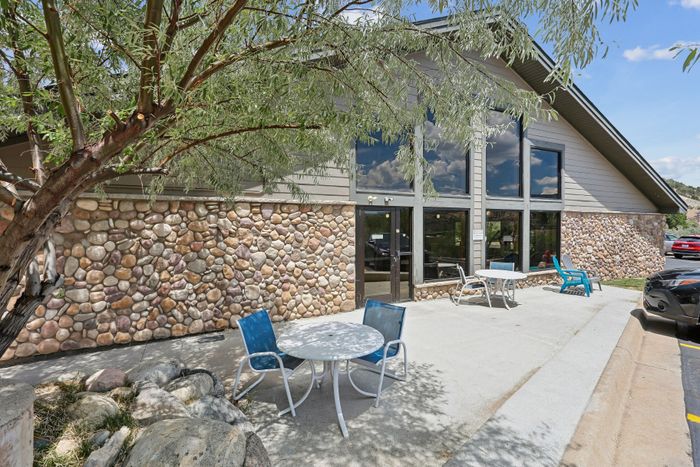 Charming outdoor patio with vibrant blue seating, nestled against a rustic stone facade and lush greenery, offering a serene gathering space under the sun.