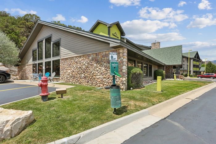 Charming apartment complex with stone exterior, modern green accents, and mountain views, featuring lush landscaping and convenient parking.