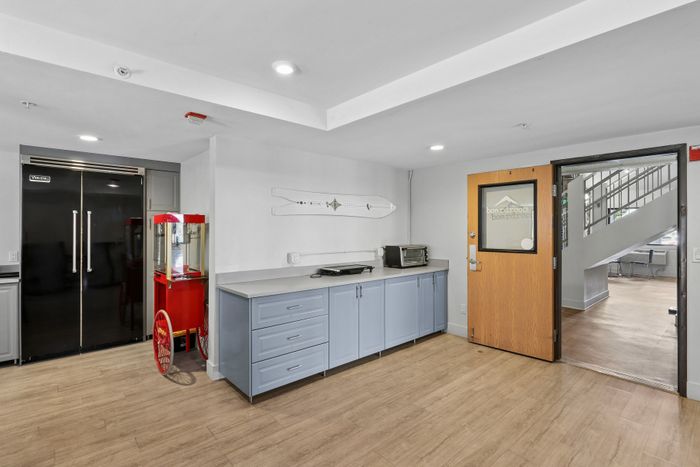 Modern multi-use room with sleek cabinetry, large refrigerator, and whimsical popcorn machine, perfect for entertaining and gatherings.