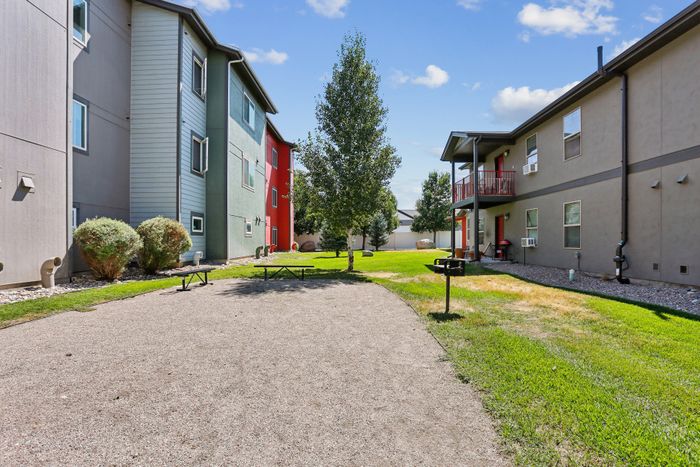 Charming outdoor view of modern apartments with colorful facades, set against a bright blue sky, featuring a lush green lawn and inviting picnic area.