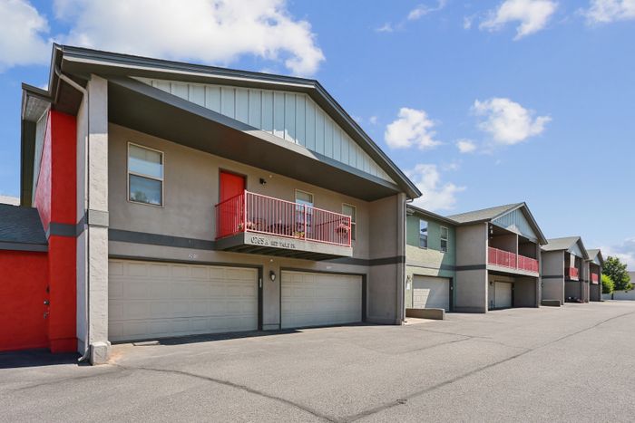 Modern row of townhouses featuring vibrant red accents, private balconies, and spacious double garages under a clear blue sky.