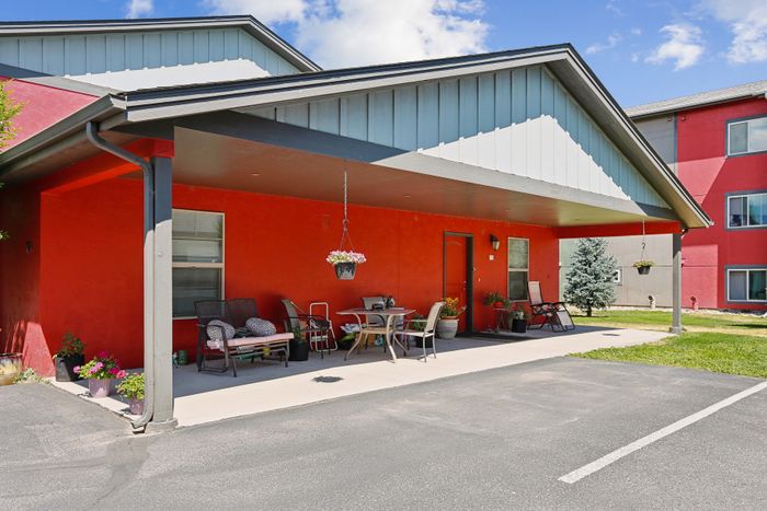 Charming apartment exterior with vibrant red walls, inviting covered patio, and stylish outdoor seating.