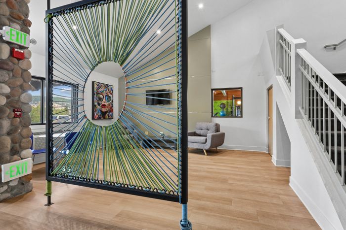 Contemporary apartment lobby showcasing artistic decor with vibrant wall art, unique string art divider, cozy seating area, and stylish staircase in a light-filled space.