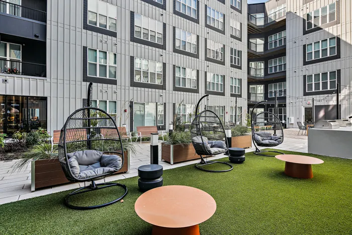 Lofts at Yard 56 cozy patio with hanging chairs and tables in front of a beautiful building. Perfect spot to relax and enjoy the outdoors.