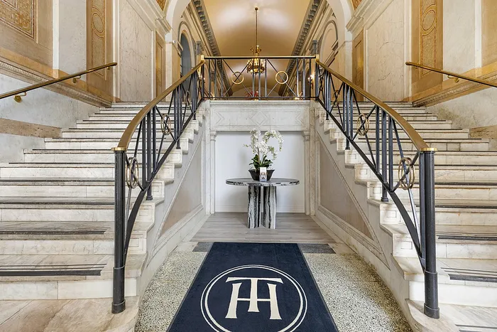 Elegant marble staircase with decorative railings leading to a luxurious hallway adorned with a chandelier and modern decor.