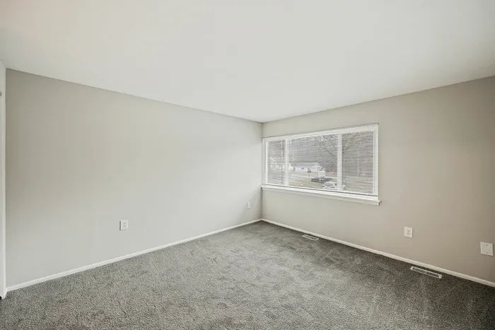 Modern room with neutral walls, plush carpeting, and large window offering ample natural light.