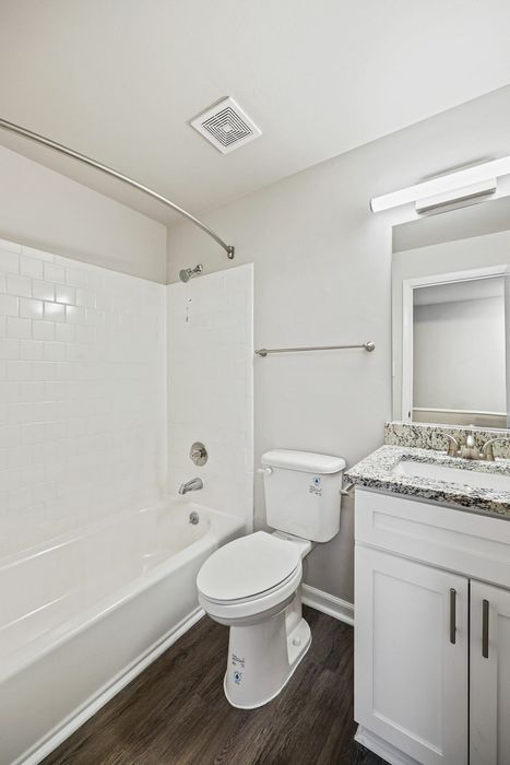 Bright, modern bathroom featuring a bathtub, tiled walls, sleek vanity with a granite countertop, and wood flooring.