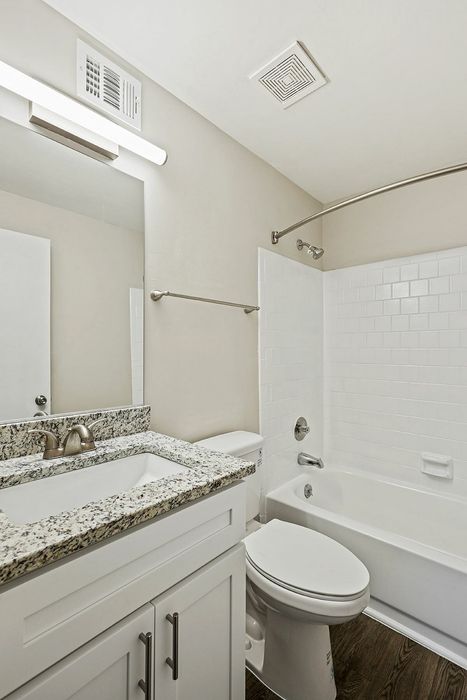 Elegant bathroom with modern granite countertop, sleek fixtures, and a tiled bathtub.