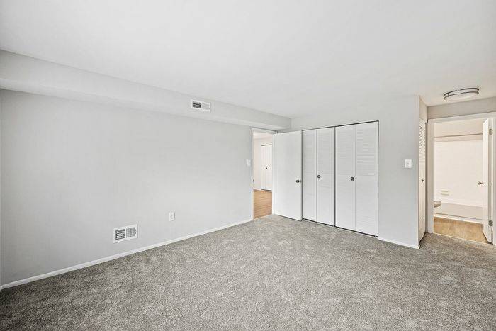 Spacious bedroom with plush carpeting, white walls, and large closet space, leading to a bathroom.