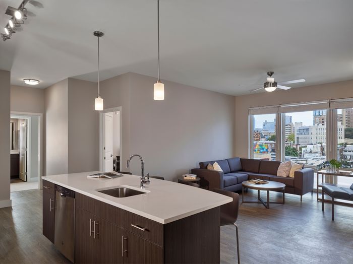 the simon at founders row. kitchen island with sink overlooking living area with couch, tables, and hardwood floors.