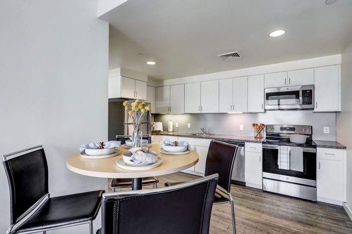 campus crossings at college row model kitchen and dining area with stainless steel appliances, stove, microwave and table top with three chairs. lancaster pa franklin & marshall