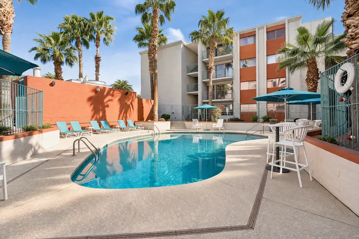 Inviting apartment complex pool area with vibrant lounge chairs, umbrellas, and palm trees, perfect for relaxation under the sun.