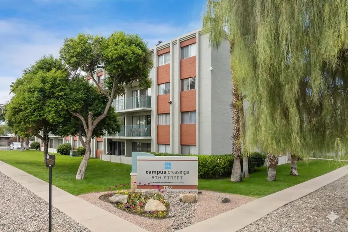 Charming apartment building at Campus Crossings 8th Street, surrounded by lush greenery and a welcoming landscape on a sunny day.