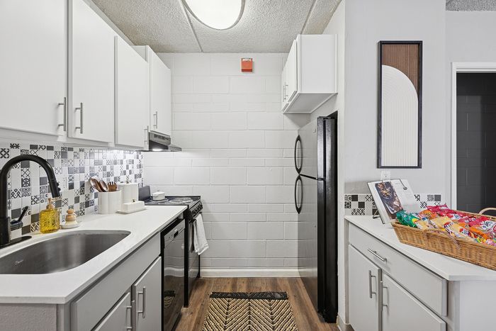 Modern kitchen with sleek white cabinetry, stylish patterned backsplash, and elegant wood flooring for a chic apartment ambiance.