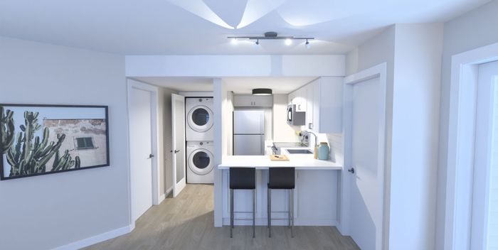 Modern apartment kitchen with sleek white cabinetry, stainless steel appliances, and cozy breakfast bar. Features in-unit stacked washer and dryer.