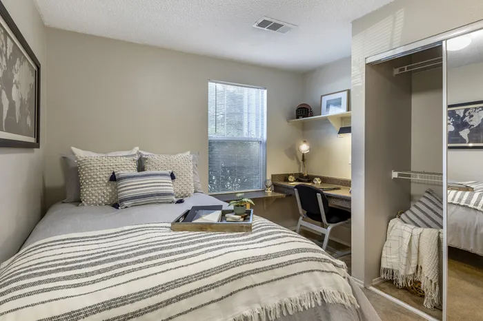 Inviting bedroom with stylish decor, cozy bed with decorative pillows, and functional workspace under natural light.