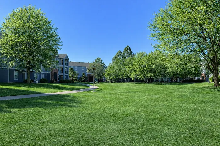 Charming apartment complex nestled in a lush green landscape with vibrant trees and a serene pathway.