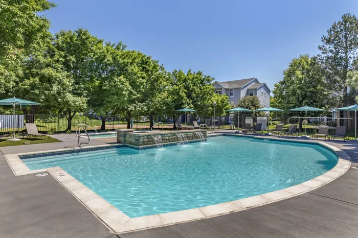 Lush apartment complex pool area with sparkling water, surrounded by greenery and comfortable sun loungers, offering a tranquil and refreshing retreat.