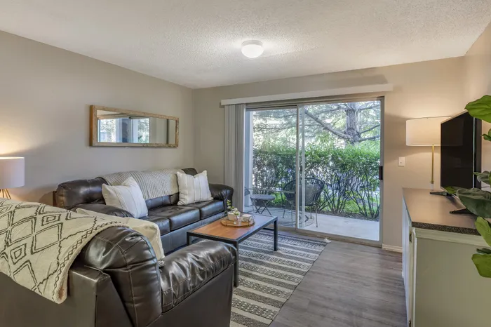 Inviting living room with cozy sofas, large mirror, and glass doors opening to a lush outdoor patio.