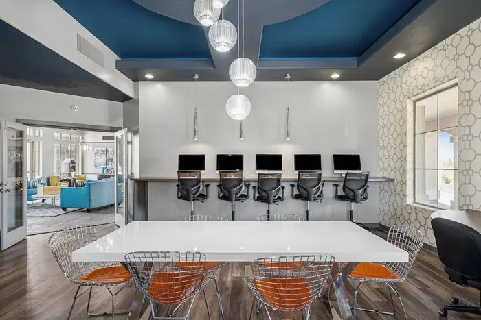 Modern apartment community workspace featuring sleek computers, stylish seating, and contemporary decor under a striking blue ceiling.
