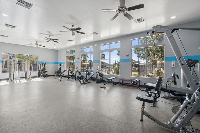 Bright and spacious fitness center with modern gym equipment, large windows offering scenic views, and ceiling fans for comfort.