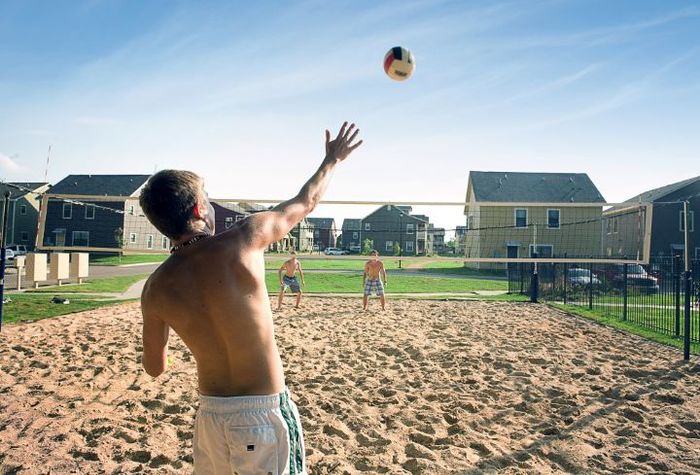 Vibrant outdoor sand volleyball court with players enjoying a sunny day, surrounded by modern residences.