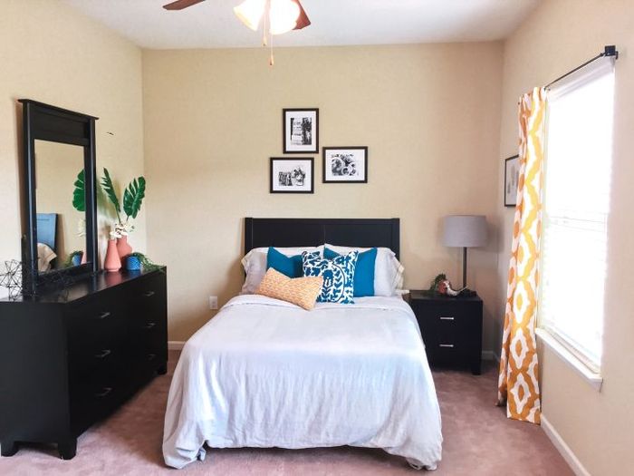 Charming bedroom with elegant decor, featuring a cozy bed with colorful pillows, stylish dresser, and bright natural light from a large window.