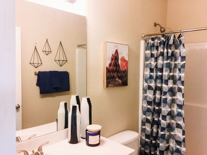 Inviting bathroom with stylish geometric wall decor, vibrant artwork, and a modern blue-patterned shower curtain. Elegant countertop accessories add a touch of luxury.