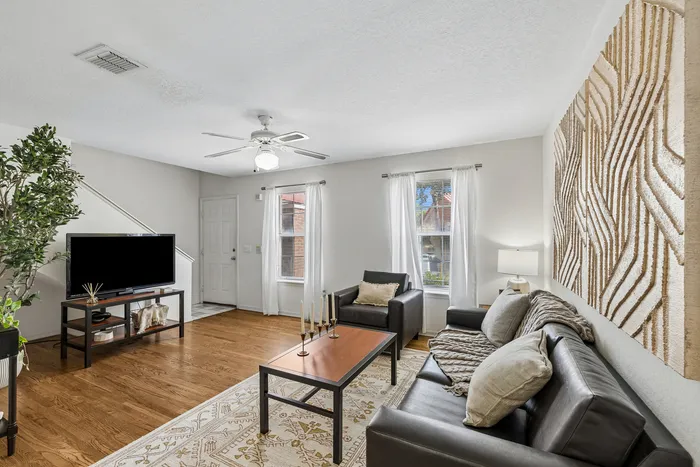Inviting living room with elegant hardwood floors, modern furniture, and natural light from large windows, creating a cozy atmosphere.