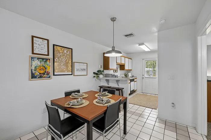 Inviting dining area in a modern kitchen featuring chic wall art, stylish table setting for four, and sleek cabinetry with natural light pouring in from the glass door.