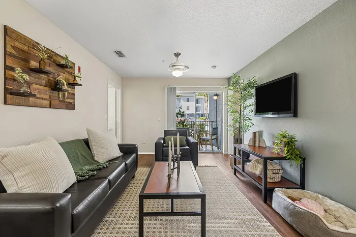 Bright and inviting living room with modern leather seating, chic decor, and greenery, opening to a cozy balcony with outdoor seating.