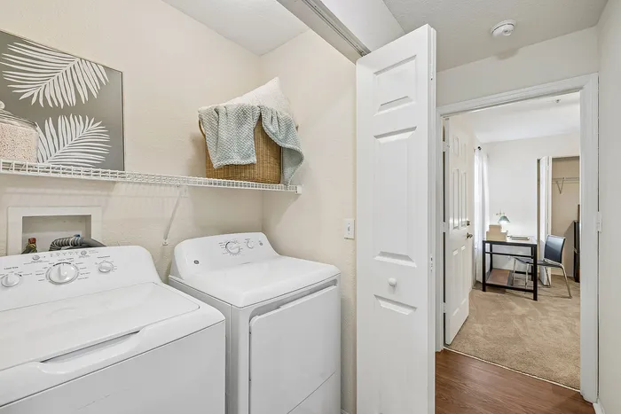 Modern laundry room featuring sleek white appliances and a convenient workspace in the adjoining room.