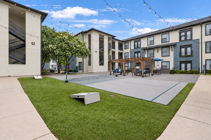 Charming courtyard view featuring modern apartments, vibrant green space, stylish pergola, and cozy seating area under string lights.