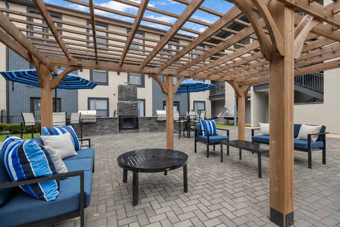 Charming outdoor patio featuring cozy seating under a wooden pergola, complemented by a modern fireplace and inviting hammocks, perfect for relaxation and entertaining.