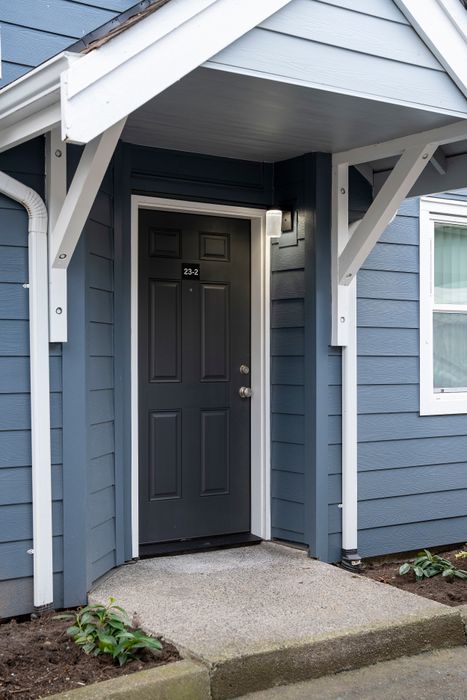Inviting front entrance of a modern apartment with a sleek black door and blue siding.