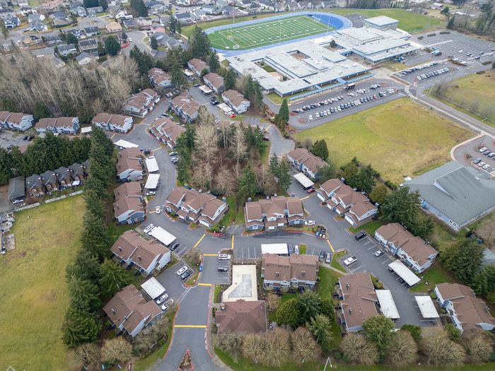 Aerial view of a peaceful residential community bordered by lush greenery and a nearby school sports facility.