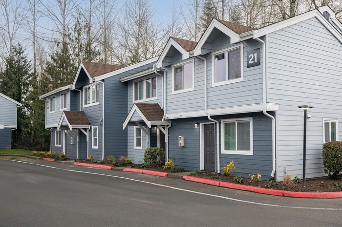 A picturesque two-story townhouse with blue siding, white trim, and neatly landscaped surroundings.