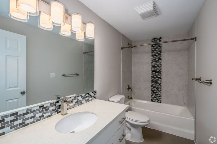 Elegant bathroom featuring modern lighting, sleek vanity with mosaic tile backsplash, and a stylish bathtub with an eye-catching tile accent wall.