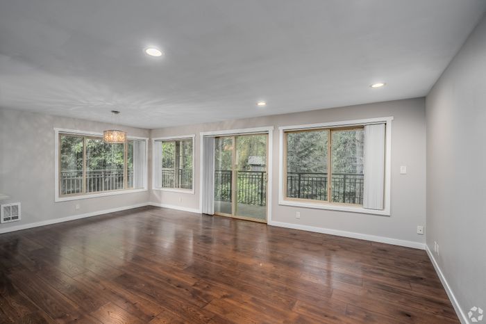 Spacious living room with elegant hardwood floors and large windows offering serene views of lush greenery.