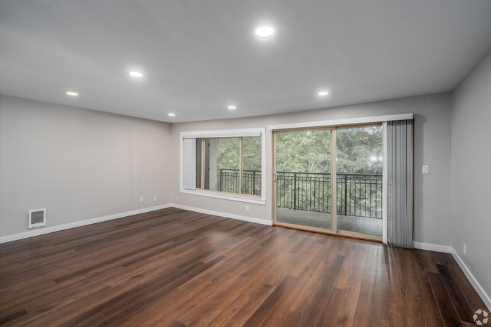 Bright and spacious living room with elegant hardwood floors, large windows, and a charming balcony view of lush greenery.