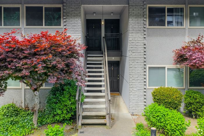 Charming apartment entrance with modern gray brick facade, elegant stairway, and vibrant landscaping.