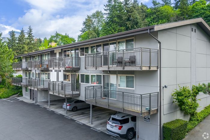 Charming three-story apartment building with spacious balconies surrounded by lush greenery and ample parking space.