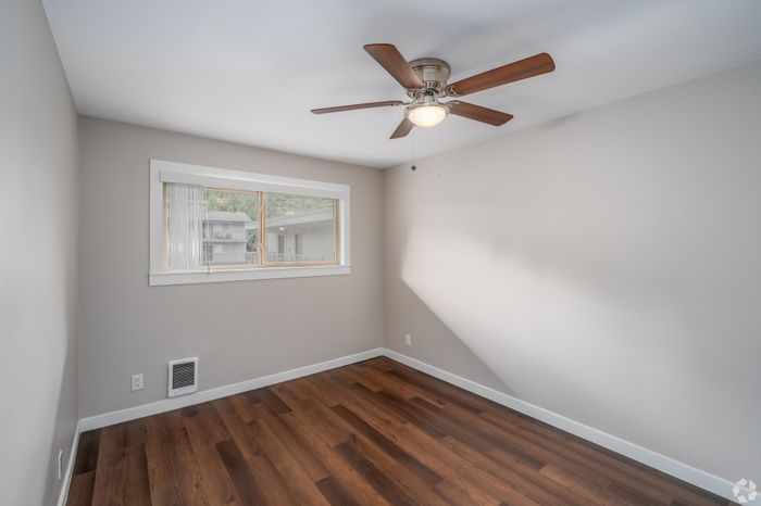 Bright bedroom with elegant hardwood flooring, a modern ceiling fan, and a large window offering natural light.