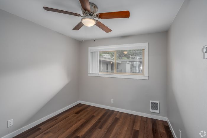 Bright and cozy bedroom featuring beautiful wood flooring, a ceiling fan, and a large window offering natural light.