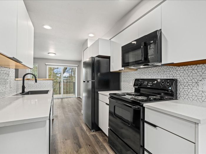 Sleek, modern kitchen with black appliances, chic geometric backsplash, and bright natural light from sliding glass doors.