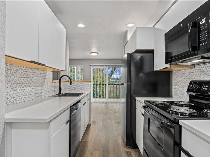 Modern kitchen with sleek white cabinetry, stylish geometric backsplash, and stainless steel appliances, offering a bright and inviting culinary space with view of the outdoor greenery through glass doors.